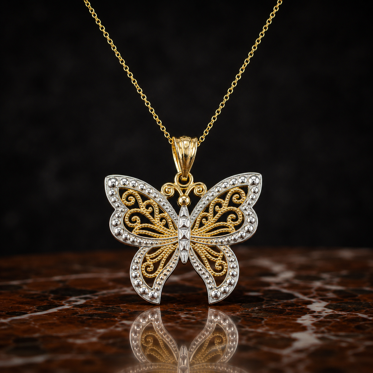A butterfly-shaped pendant necklace in yellow gold and silver-tone metal, embellished with small clear stones, displayed on a dark reflective surface against a black background.