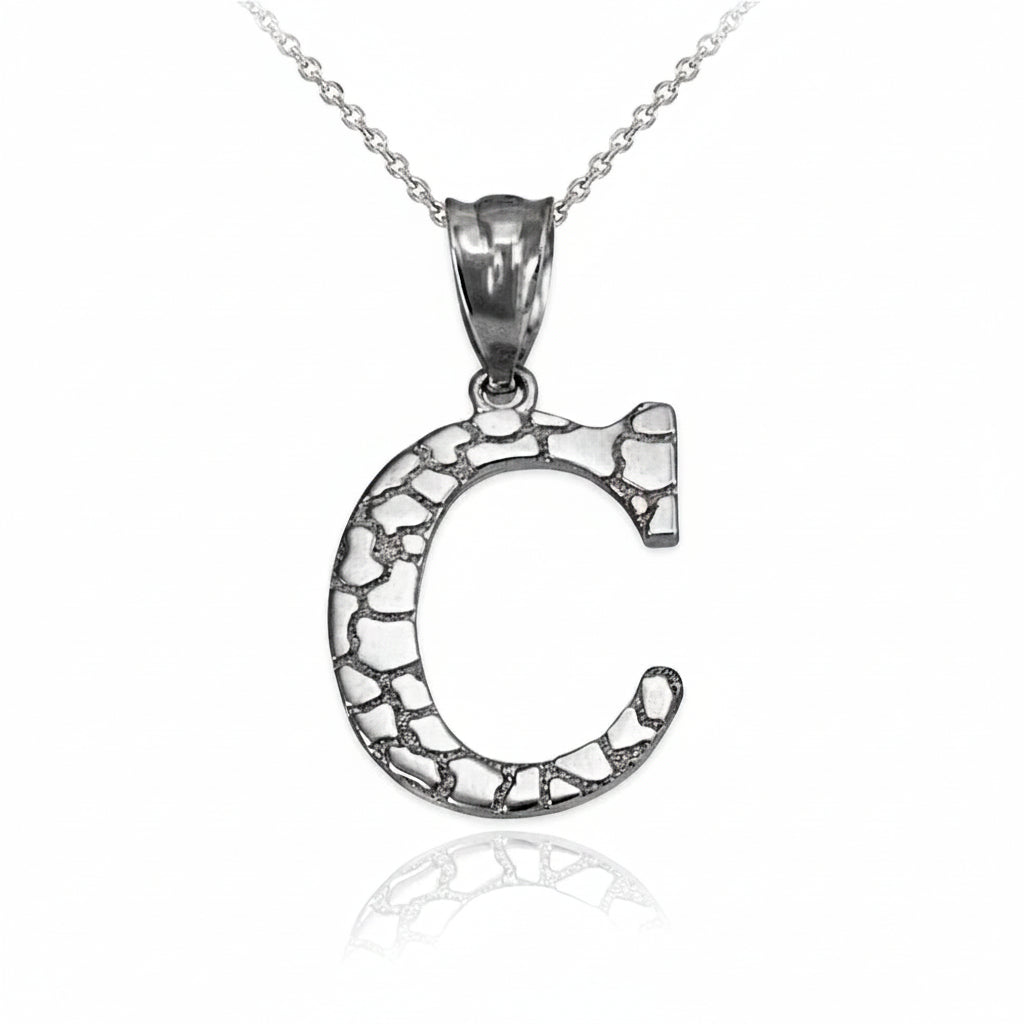A silver letter C pendant necklace with an oxidized, textured interior and a polished bail, hanging from a delicate silver chain on a white background with a soft reflection below.