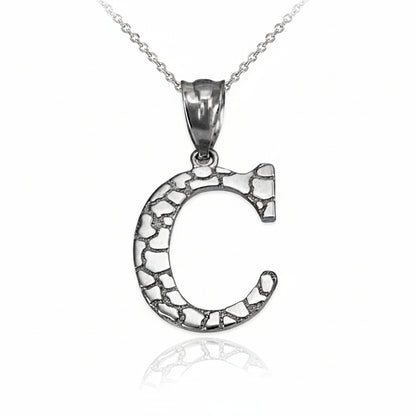 A silver letter C pendant necklace with an oxidized, textured interior and a polished bail, hanging from a delicate silver chain on a white background with a soft reflection below.
