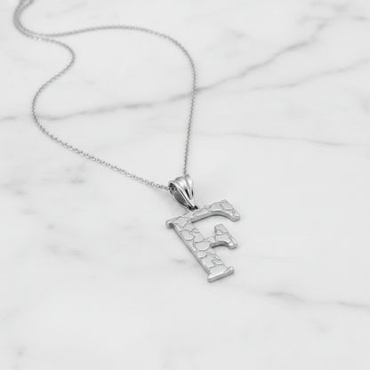 A silver initial pendant necklace featuring the letter 'F' with a textured, crackled finish, suspended from a delicate silver chain against a white background.