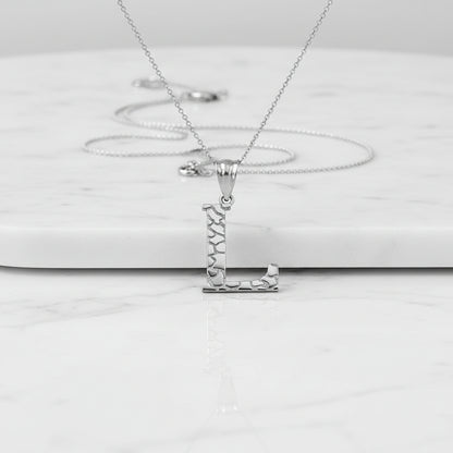 A silver initial pendant necklace featuring the letter 'L' with a textured, mosaic-like pattern on its vertical and horizontal bars, suspended from a delicate link chain against a white background with a soft reflection below.