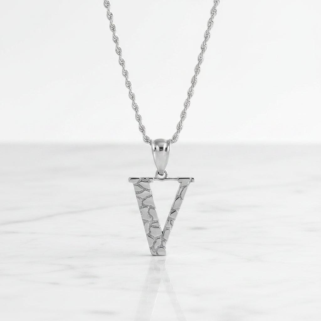Silver letter V pendant necklace with a textured, openwork design on a matching chain, shown on a white background with a soft reflection.
