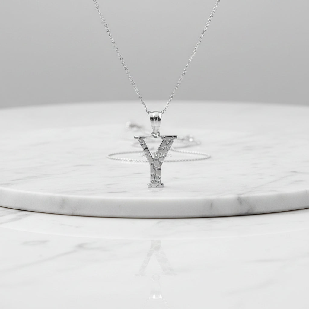 A silver initial pendant necklace featuring the letter 'Y' with a textured, cracked-glass design, suspended from a delicate silver chain on a white background with a soft reflection.