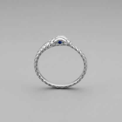 A silver snake ring with a textured scale pattern and a small blue gemstone in the center of the head, shown on a neutral gray background.