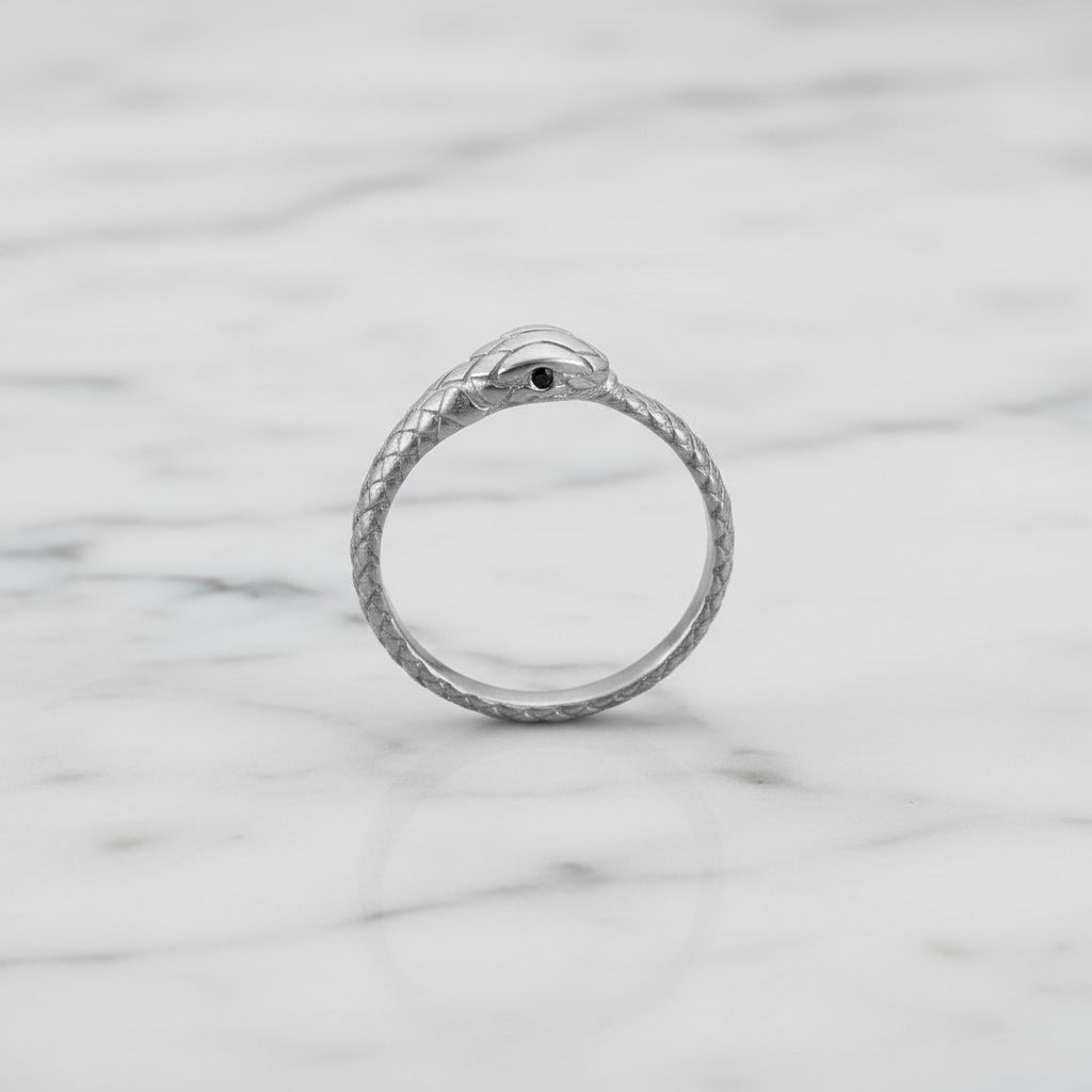 A silver snake ring with a small black eye detail, resting on a white marble surface.