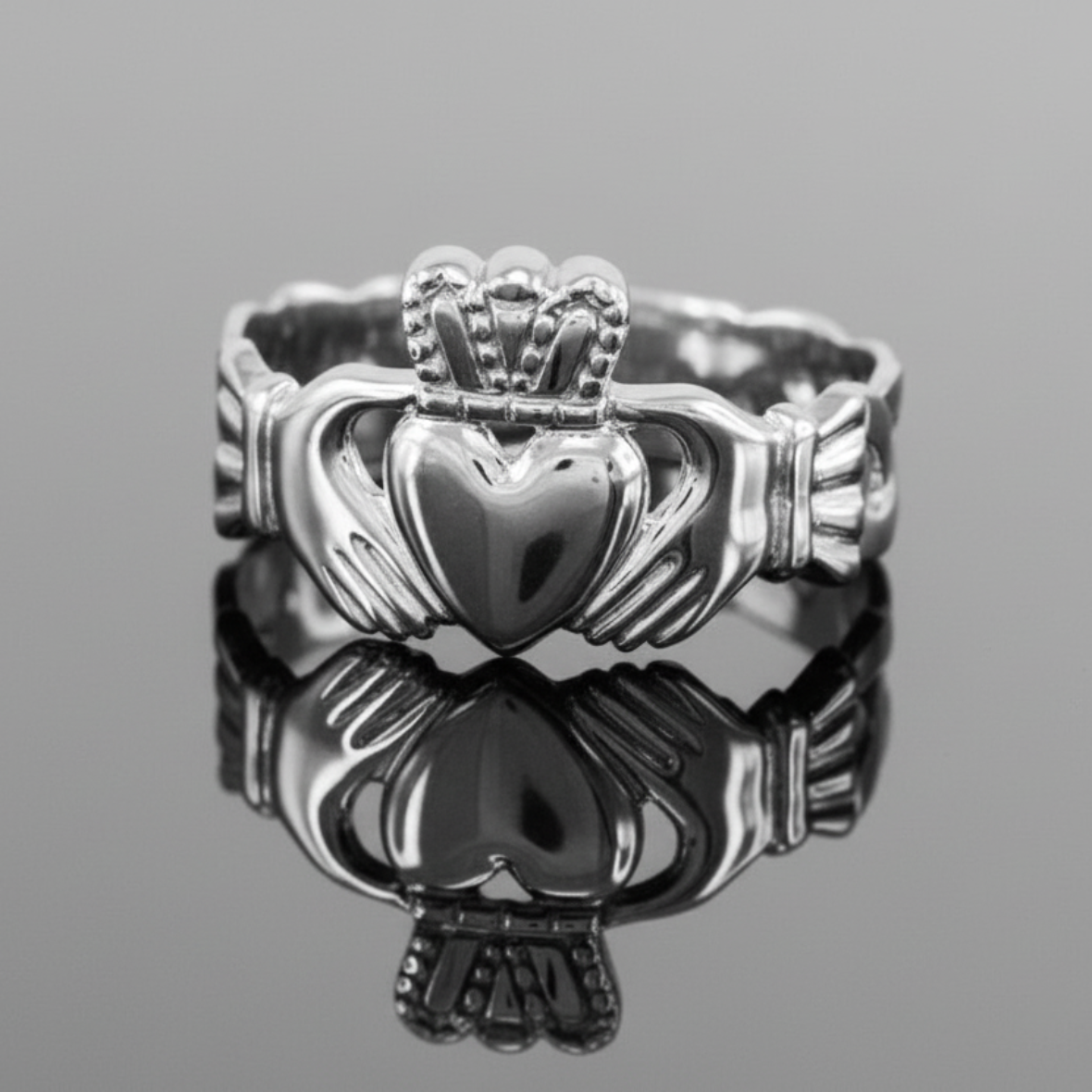Silver Claddagh ring on a reflective surface with a gray background