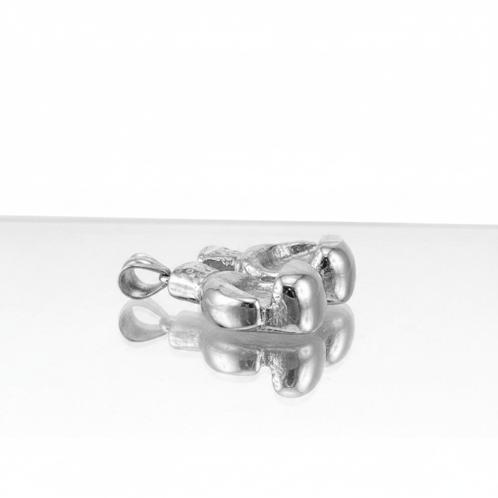 A polished silver pendant with a textured, organic, rounded design and a small loop at the top, resting on a reflective white surface against a white background.