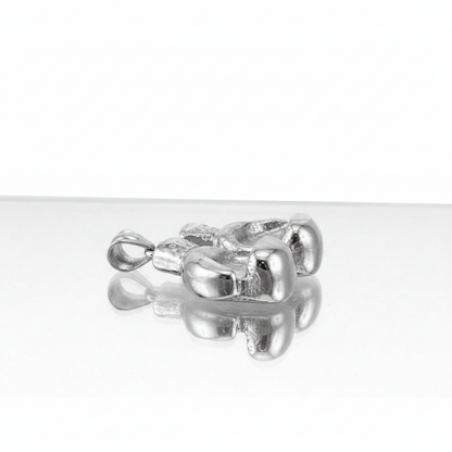 A polished silver pendant with a textured, organic, rounded design and a small loop at the top, resting on a reflective white surface against a white background.