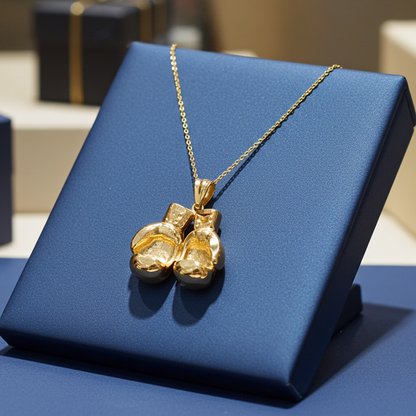 A gold pendant necklace shaped like a pair of boxing gloves, displayed on a blue jewelry stand.
