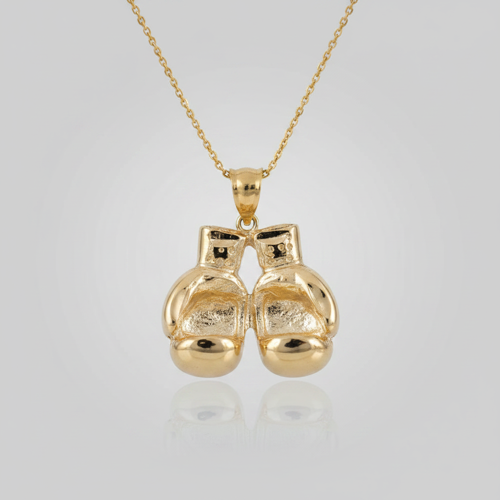 A gold pendant necklace featuring a pair of small boxing gloves hanging from a delicate gold chain, set against a light gray gradient background with a soft reflection below.