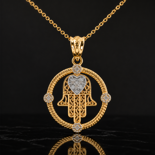 A gold Hamsa hand pendant necklace with a heart-shaped center, accented with small clear stones, shown on a black reflective background.