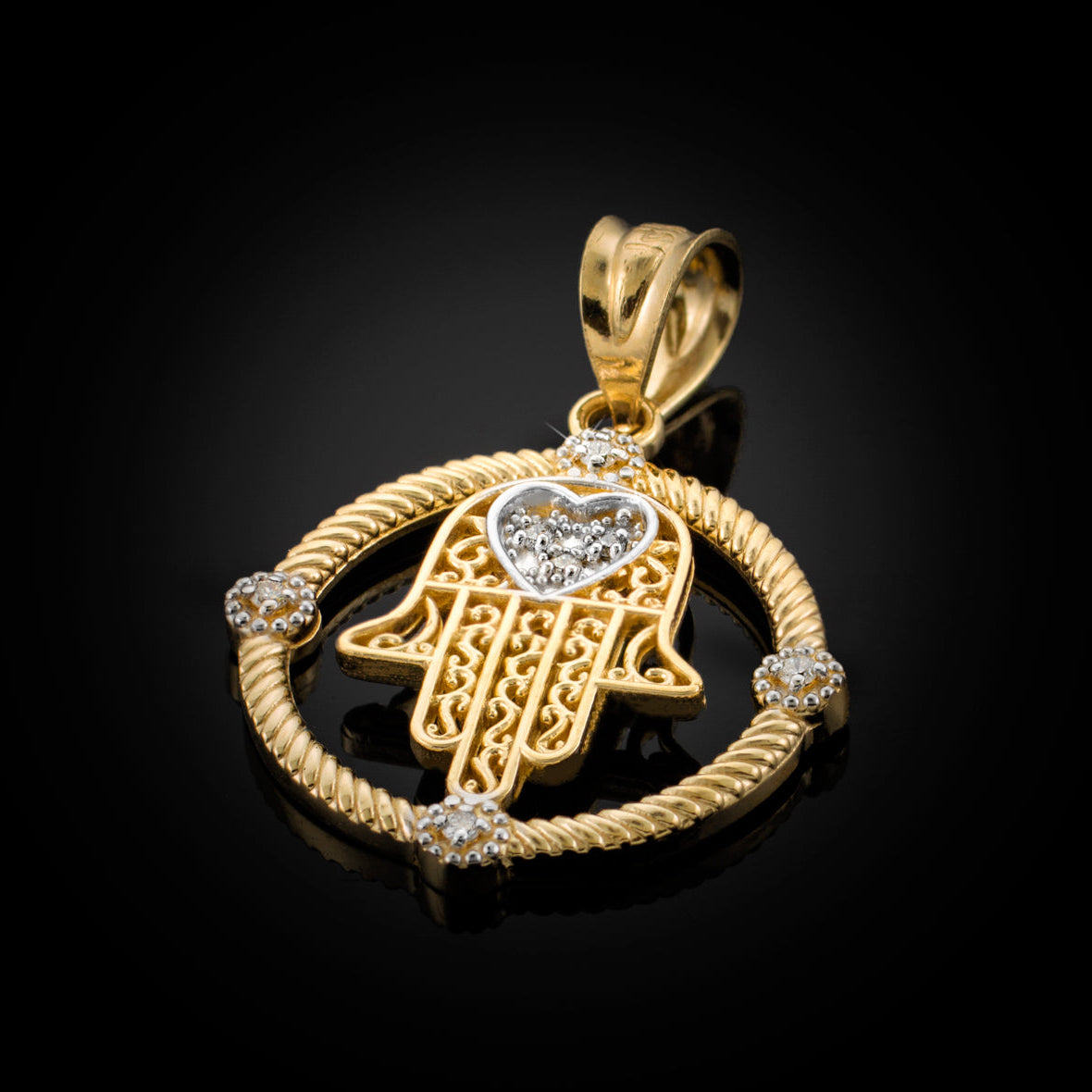 A gold Hamsa hand pendant with a heart-shaped diamond inlay, surrounded by a rope-style circular border accented with small clear stones, shown on a black reflective background.