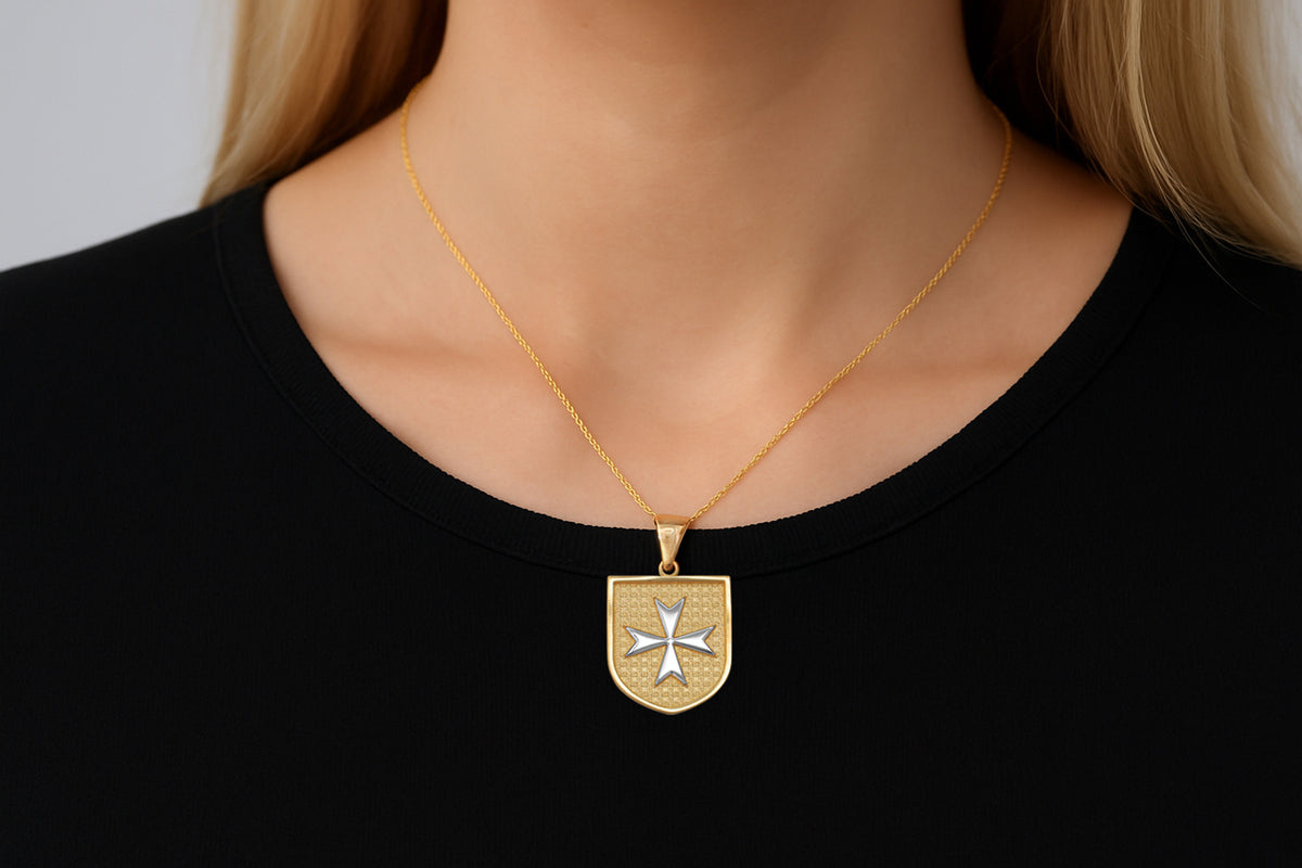 Gold necklace with a shield pendant worn by a person against a black background