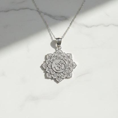 A silver-toned lotus pendant necklace featuring an Om symbol in the center, displayed on a white marble surface with soft shadows.