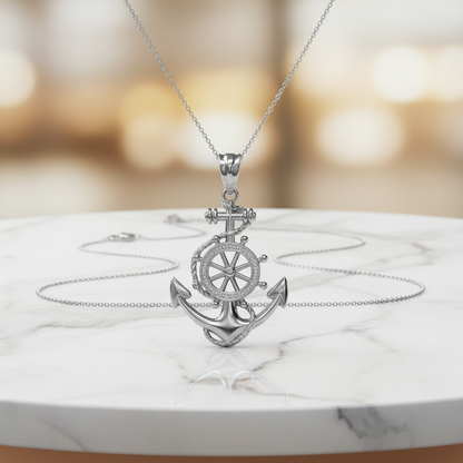 A silver anchor pendant necklace with a ship's wheel detail, displayed on a white marble surface with a blurred warm-toned background.
