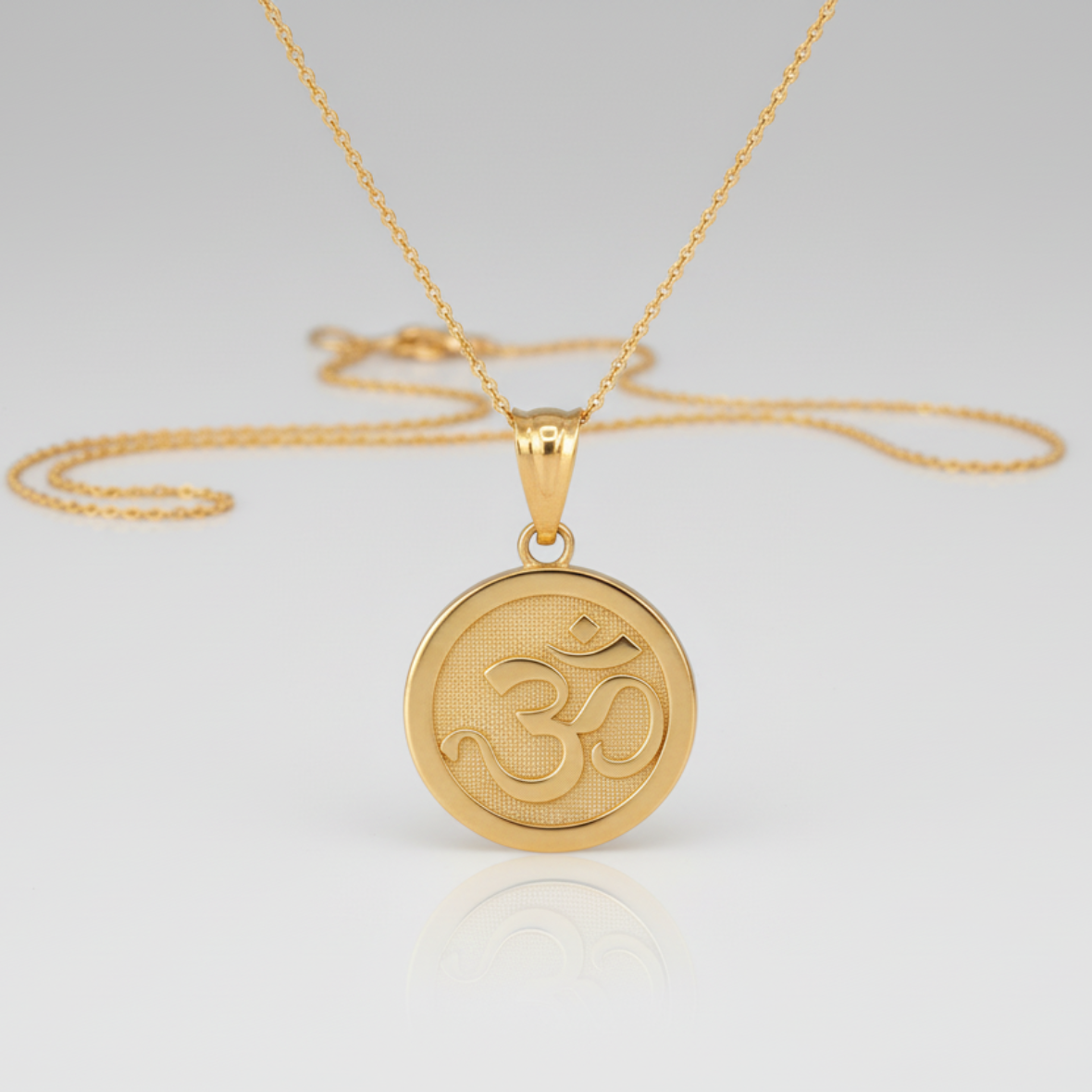 Gold necklace with a round pendant featuring the symbol 'OM' on a light gray background