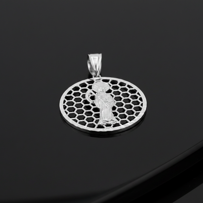 A silver pendant featuring a detailed figure of Santa Muerte set against a honeycomb circular pattern, displayed on a glossy black surface.
