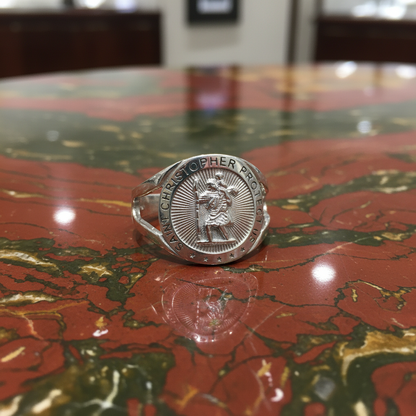 A silver ring featuring a circular medallion with an engraved figure and the text 'DE CHRISTOPHER P.