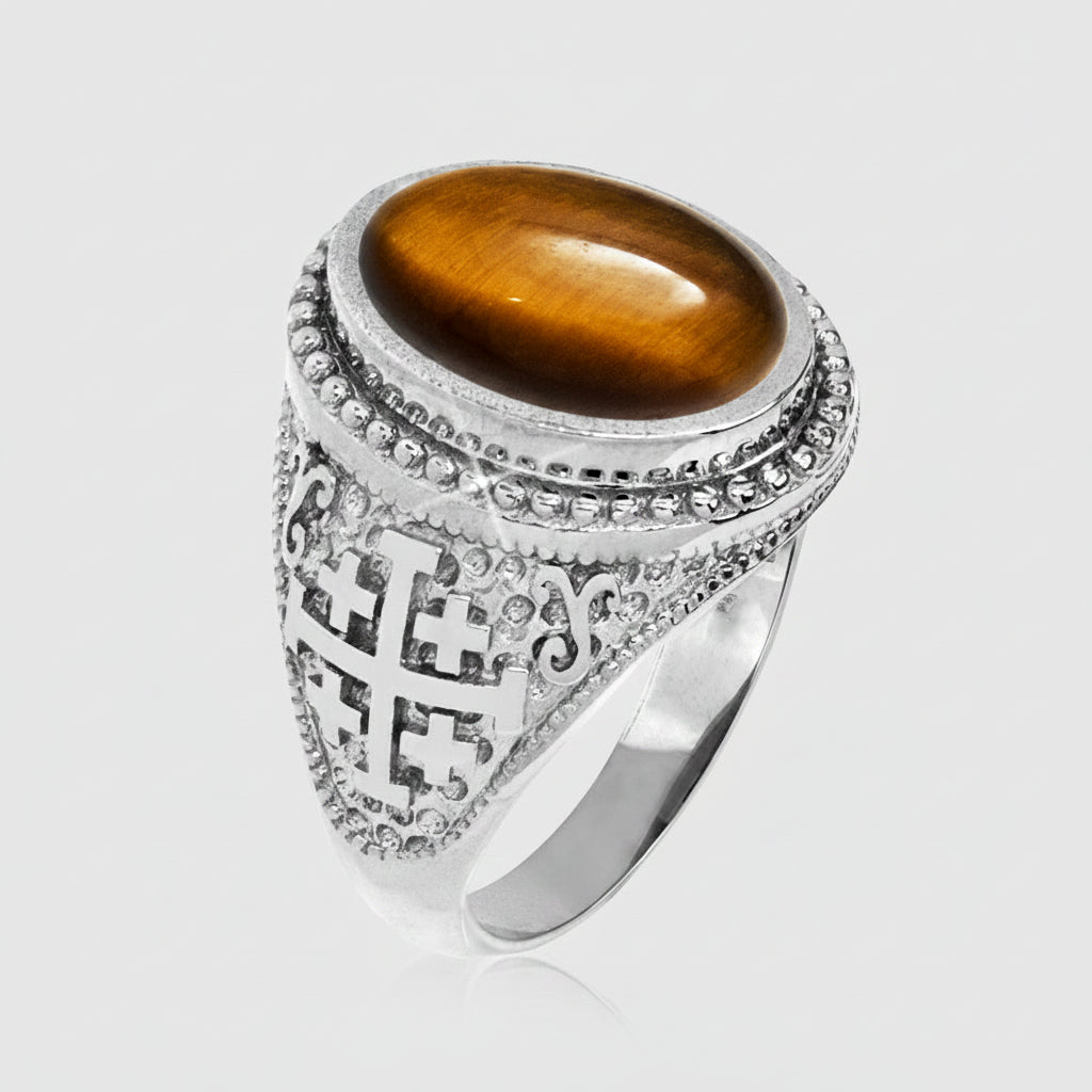 A silver-toned ring featuring a large oval brown tiger's eye stone and an ornate filigree cross motif on the shank, set against a plain white background.