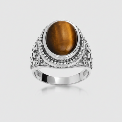 A silver-toned ring featuring a large oval brown tiger's eye stone, set in an ornate filigree-style band with small clear stones, shown on a light gray background.