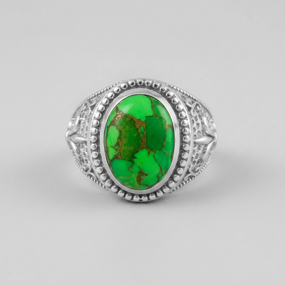 A silver ring featuring an oval green turquoise stone with natural brown matrix patterns, set in an ornate filigree-style silver band on a light gray background.