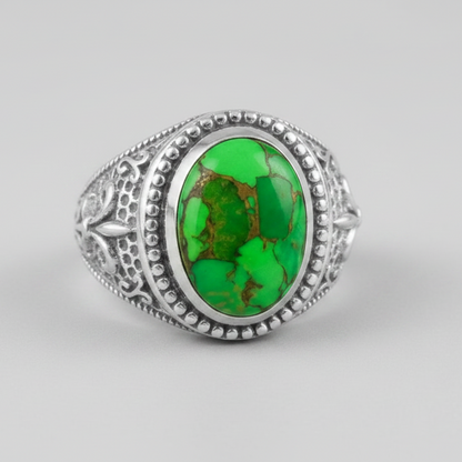 A silver ring featuring an oval green stone with brown matrix patterns, set in an ornate silver bezel with a beaded border.