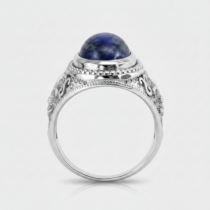 A silver-toned ring with an oval dark blue lapis lazuli stone set in an ornate filigree band, shown on a light gray background.