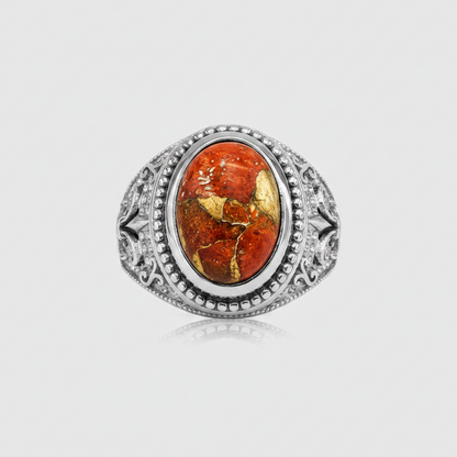 A silver-toned ring featuring an oval cabochon gemstone with a warm orange-red center and prominent gold veining, set against a light gray background.