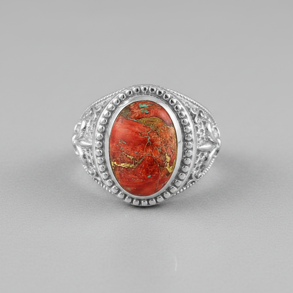 A silver ring featuring an oval red jasper stone with prominent gold and green matrix patterns, set in an ornate filigree-style silver band on a neutral gray background.