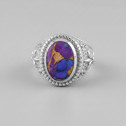 A silver ring featuring an oval cabochon stone with a vibrant purple, blue, and gold marbled pattern, set in a beaded silver bezel with ornate filigree sides.