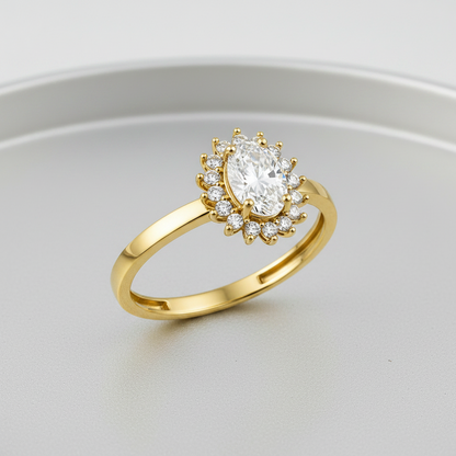 A yellow gold ring featuring an oval-cut clear center stone surrounded by a halo of small round stones, set on a polished band against a white background.
