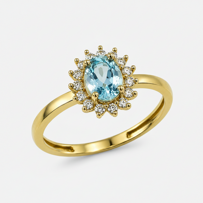 A yellow gold ring featuring an oval light aquamarine center stone surrounded by a halo of small clear cubic zirconia stones, set against a plain white background.