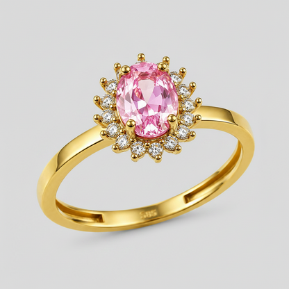 A yellow gold ring featuring an oval pink gemstone surrounded by a halo of small clear stones, shown on a clean white background.