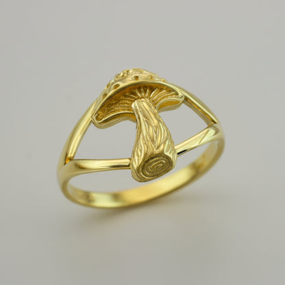 A gold mushroom-shaped ring for women displayed on a colorful textured surface with a butterfly.
