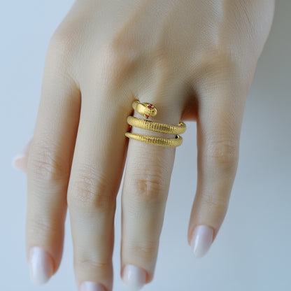 Textured yellow gold coiled snake wrap ring with ruby gemstone eyes worn on finger.