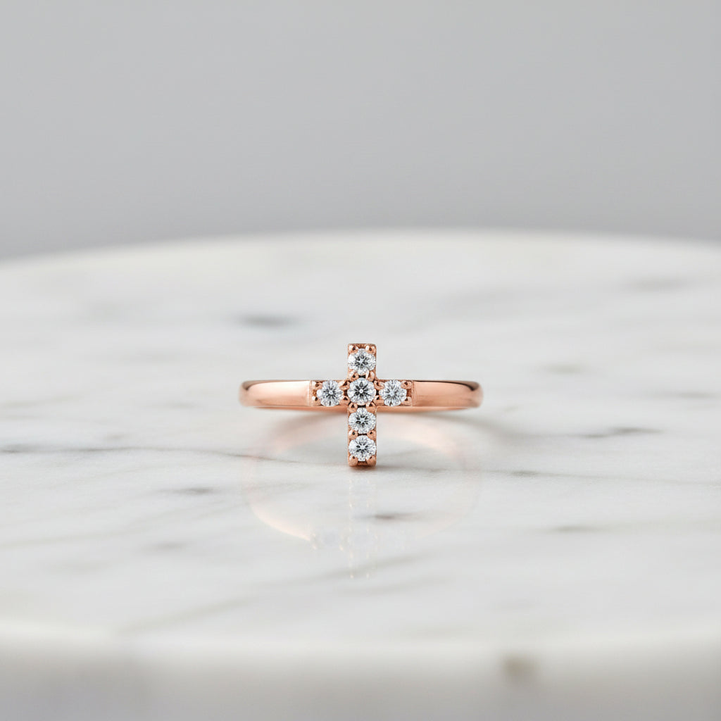 A rose gold ring featuring a small cross-shaped cluster set with clear gemstones, shown on a clean white background.