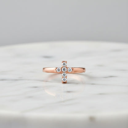 A rose gold ring featuring a small cross-shaped cluster set with clear gemstones, shown on a clean white background.