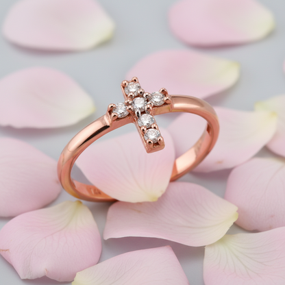 A rose gold ring with a cross-shaped setting set with small clear gemstones, resting on scattered pale pink rose petals.